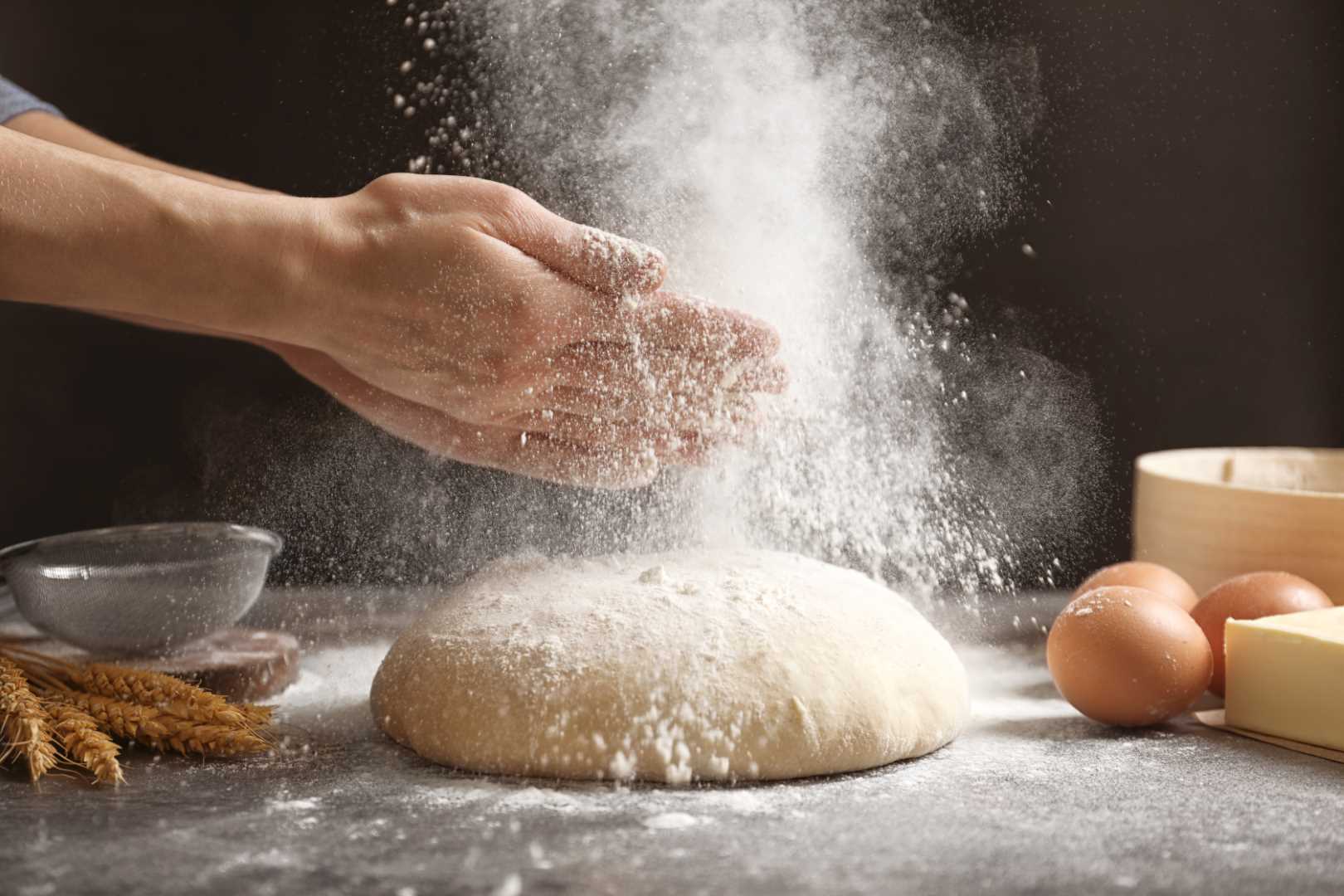 Woman clapping hands and sprinkling flour over fresh dough on table